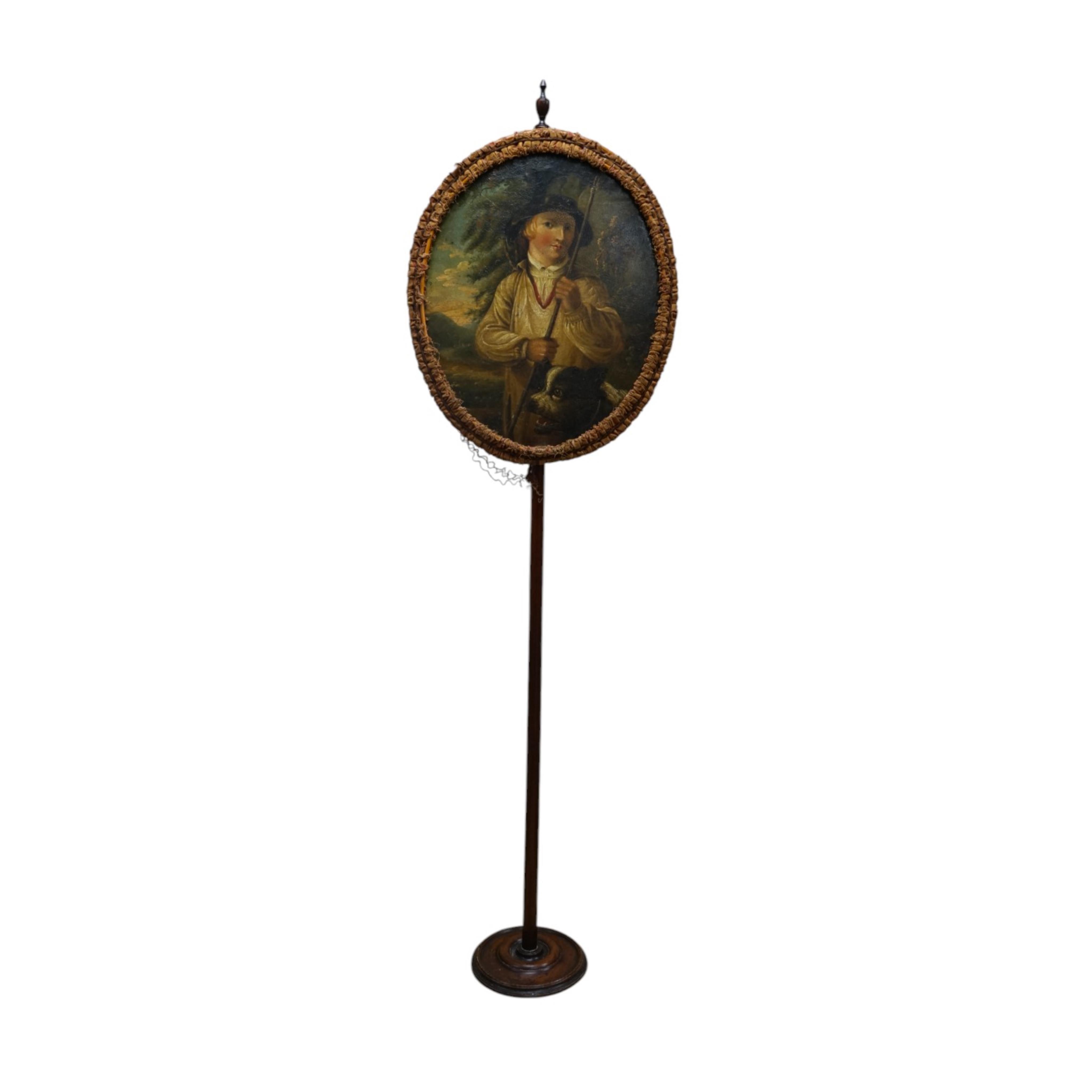 An oval Regency fire screen painting of a shepherd boy with his dog and a painting verso of ephemera, the screen edged with rushed ribbon fixed to a simple mahogany stand. 130cm high. Condition - paintings crazed and rib